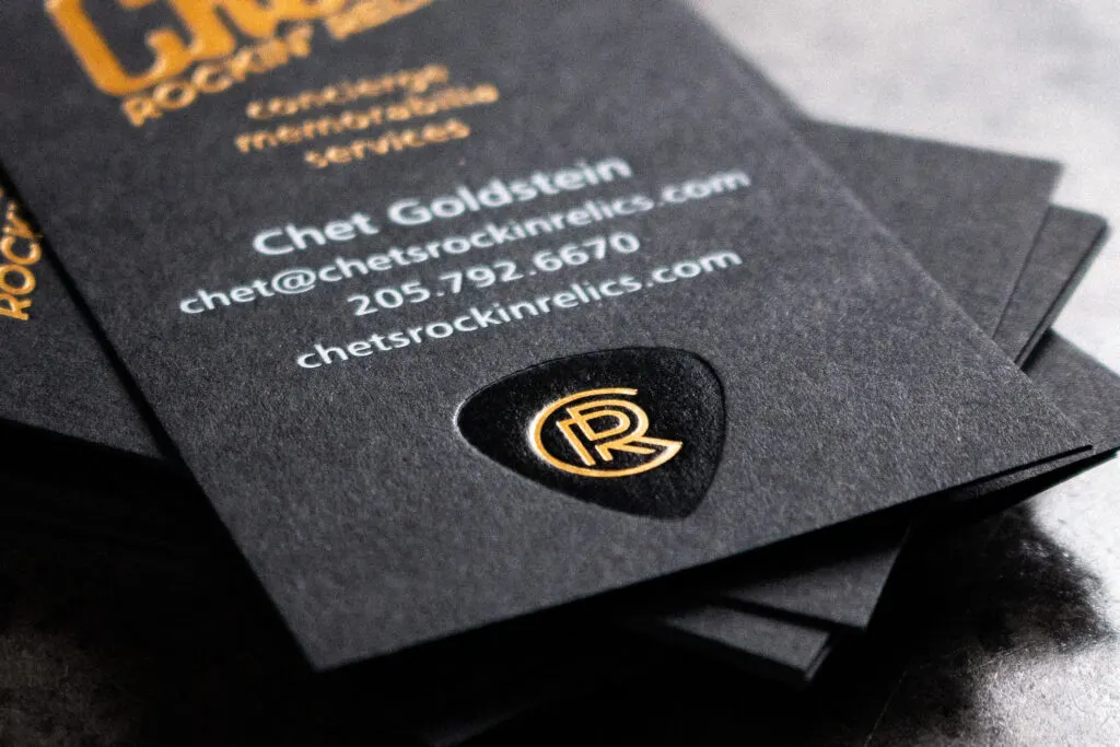 Detail of triple foil stamping showing white, gold, and black foil layers on textured black stock
